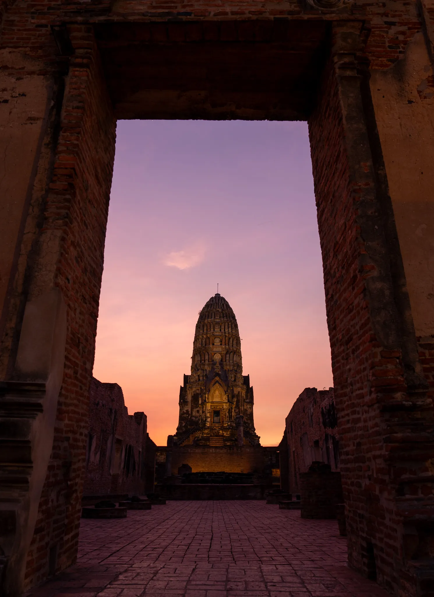 The main prang of Wat Ratchaburana, Ayutthaya, seen through the ruins of a temple entrance during twilight.