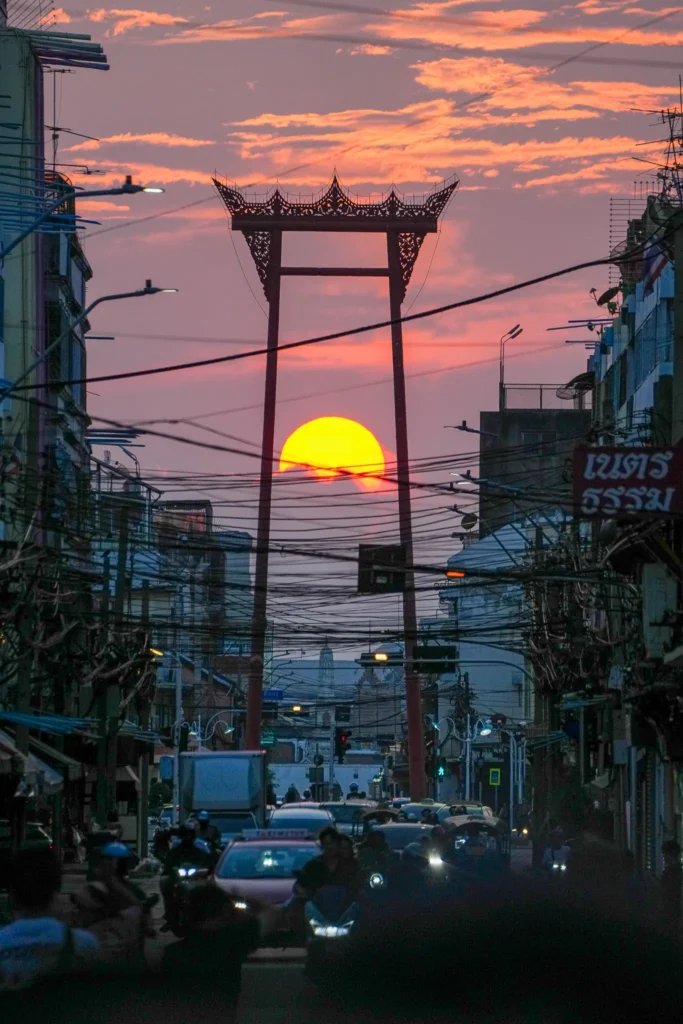 A beautiful sunset framing the historic Giant Swing and bustling evening street traffic in Bangkok, Thailand.