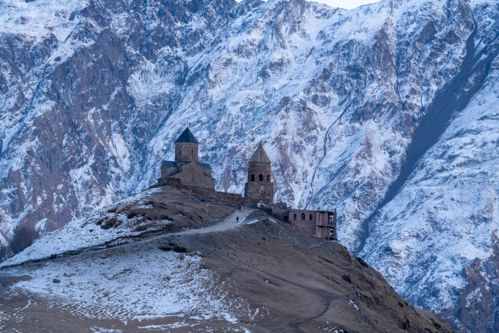The historic Gergeti Trinity Church standing prominently on a hilltop surrounded by massive snow-capped Caucasus mountains during winter in Georgia.