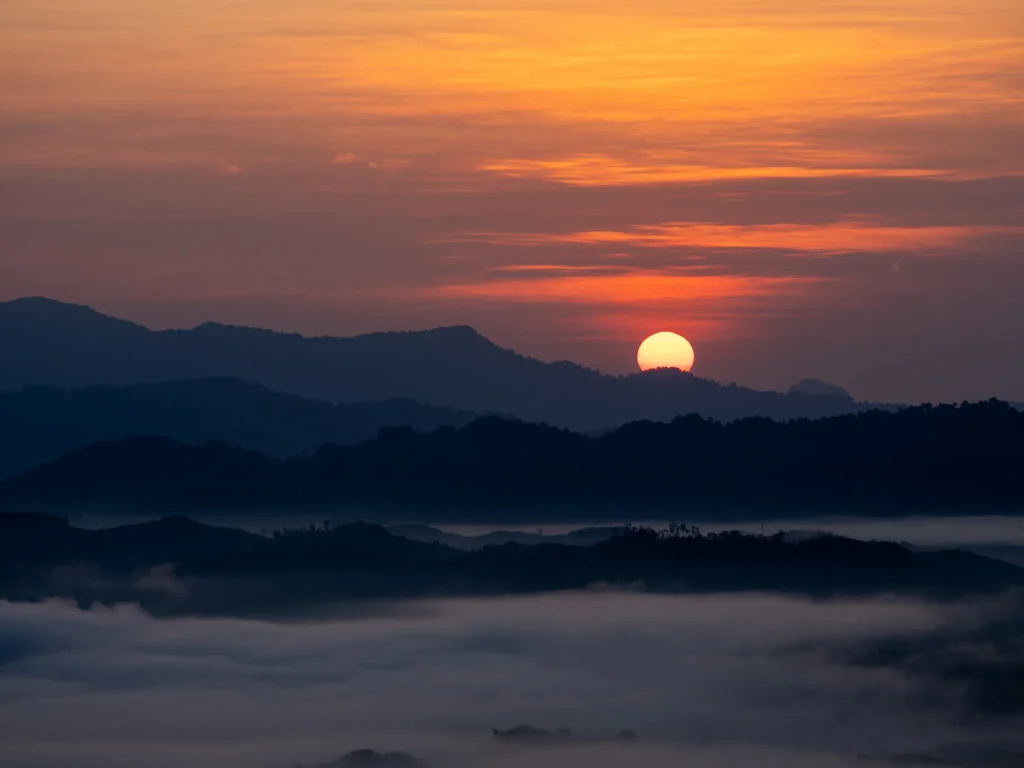 แสงเช้าที่เขาไข่นุ้ย กับภาพที่ไม่ต้องการโปรแกรมแต่งสี A bright glowing sun rising beautifully over layers of dark mountain ridges and a thick sea of morning mist in the valley.